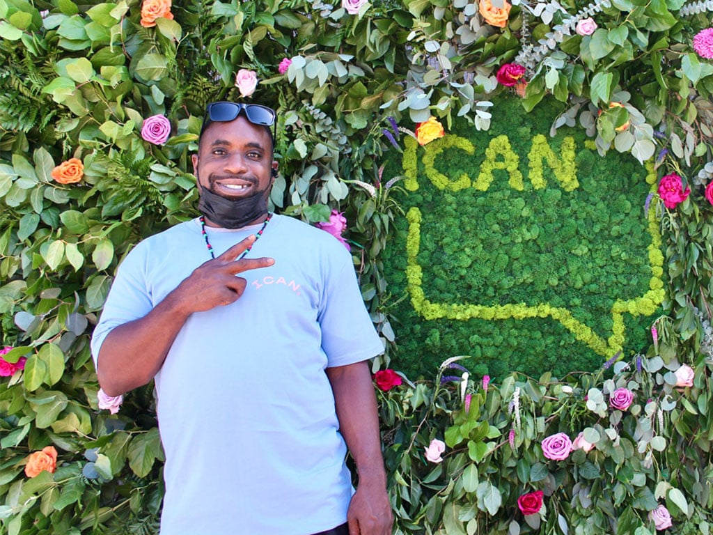 young man standing in front of a sign that says ICAN